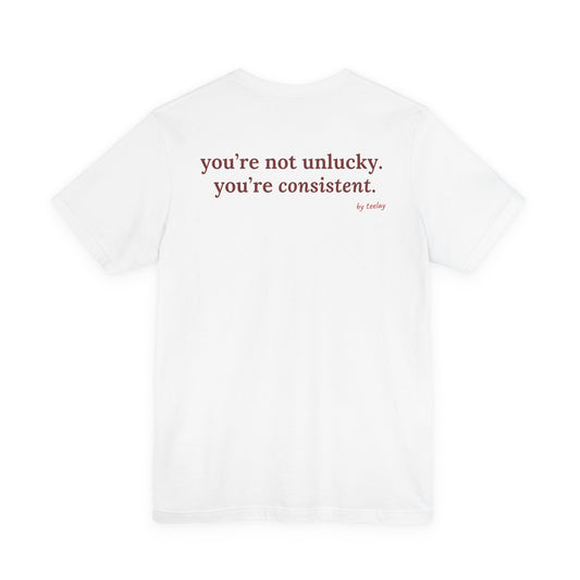 Woman from behind wearing a white oversized t shirt with "You're Not Unlucky. You're Consistent." printed on the back