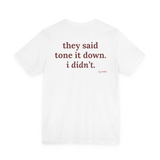 Woman from behind wearing a white oversized t shirt with "They Said Tone It Down. I Didn't." printed on the back