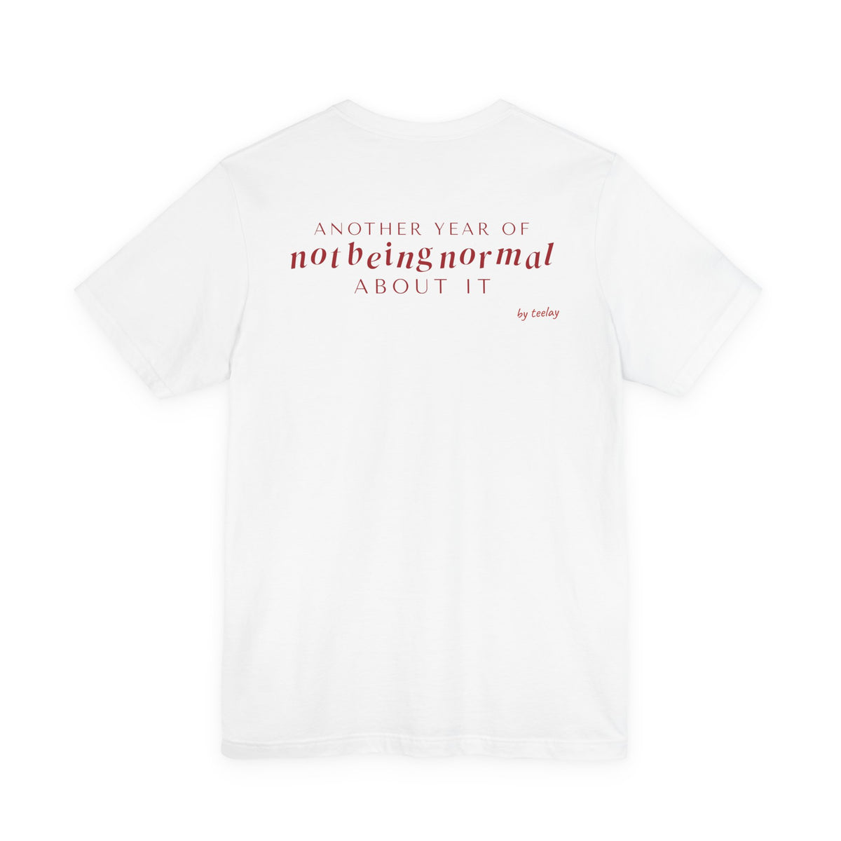 Back of a white t shirt with Another Year Of Not Being Normal About It printed in red