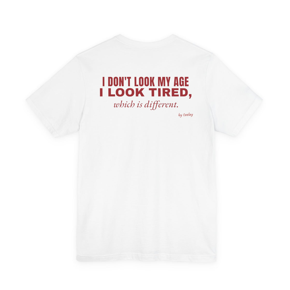 Back of a white t shirt with I Don't Look My Age I Look Tired Which Is Different printed in red