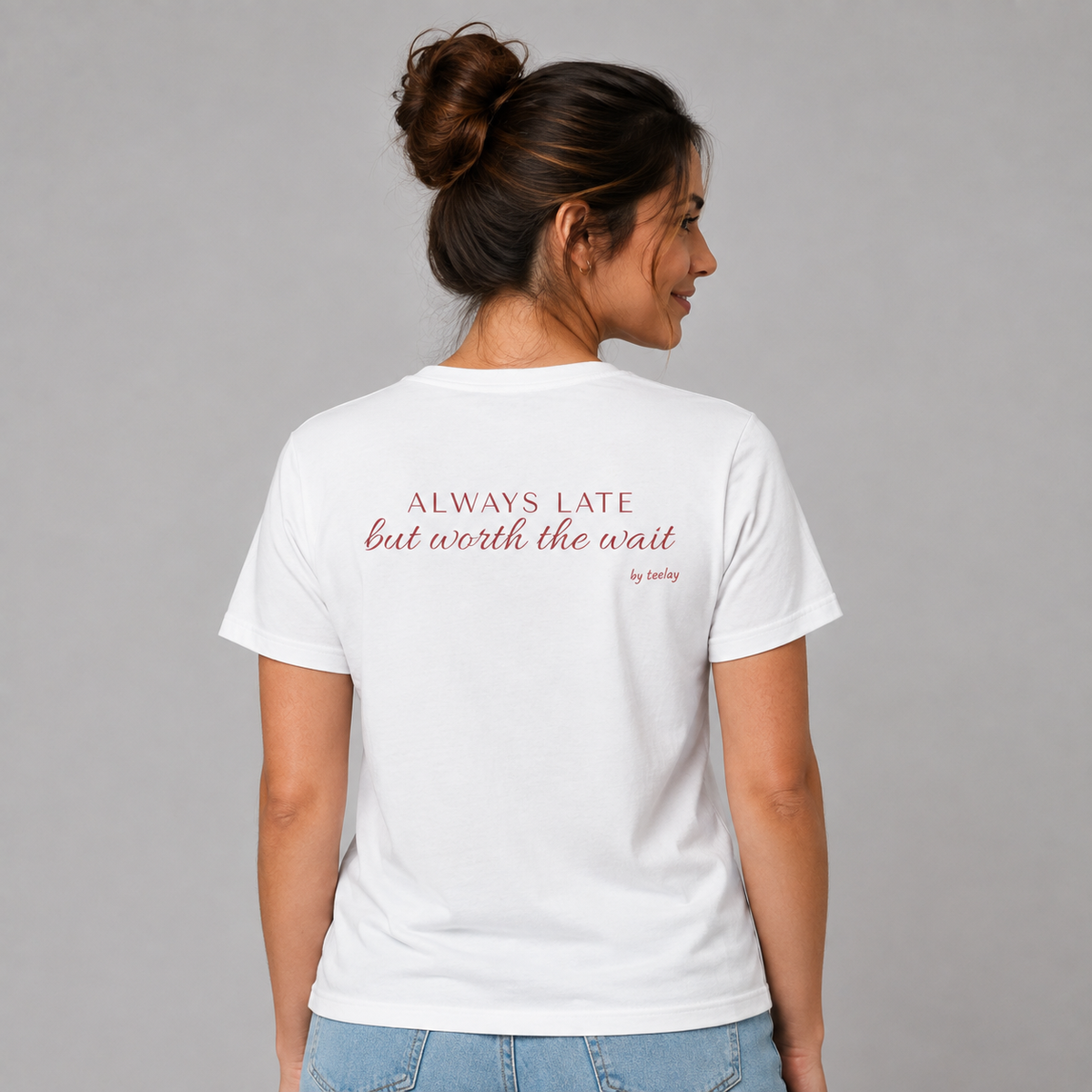 Woman wearing a white graphic tee with Always Late But Worth The Wait printed on the back, rear view