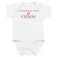 White baby bodysuit with Powered By Milk & Chaos printed in red on the front