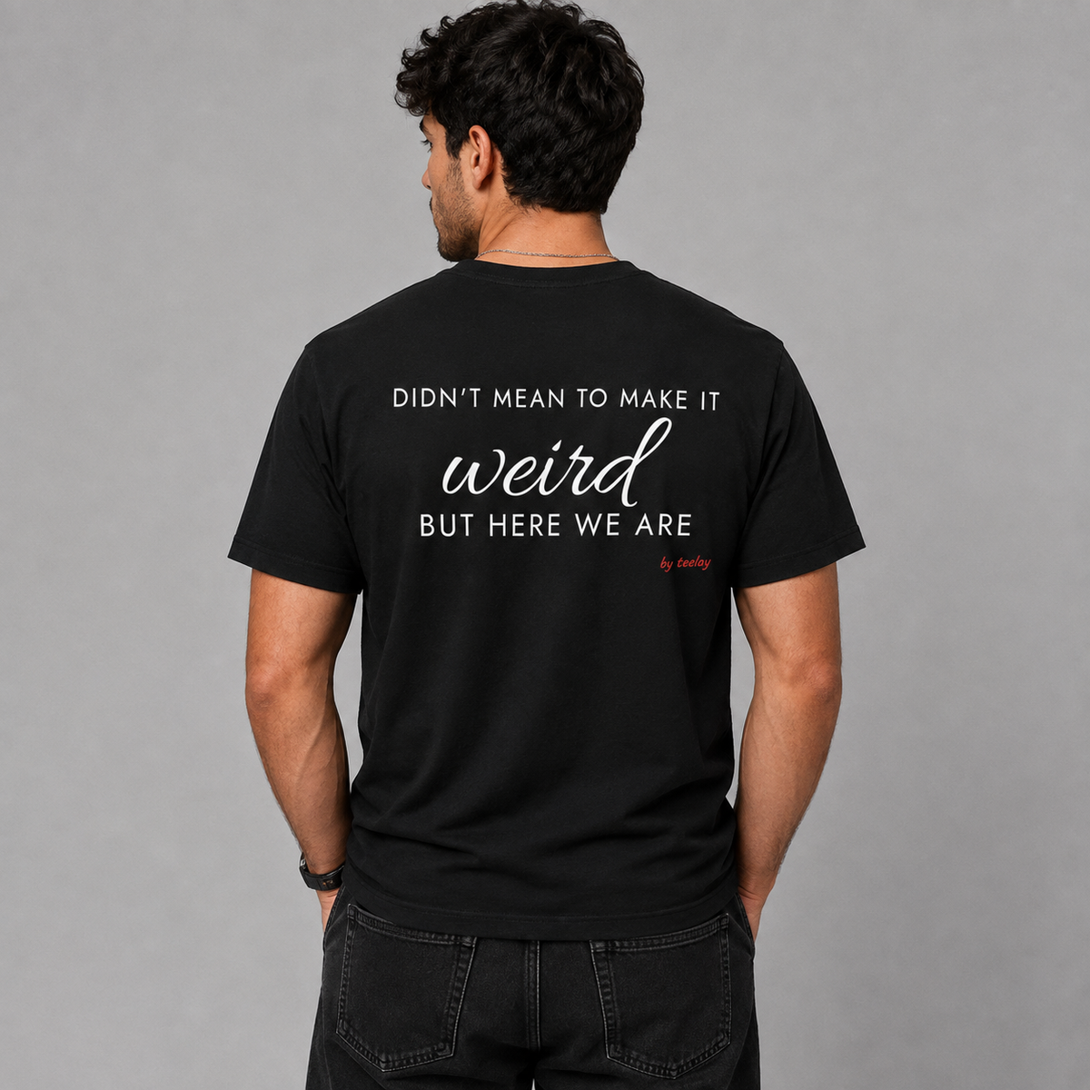 Man from behind wearing a black t shirt with Didn't Mean To Make It Weird But Here We Are printed on the back