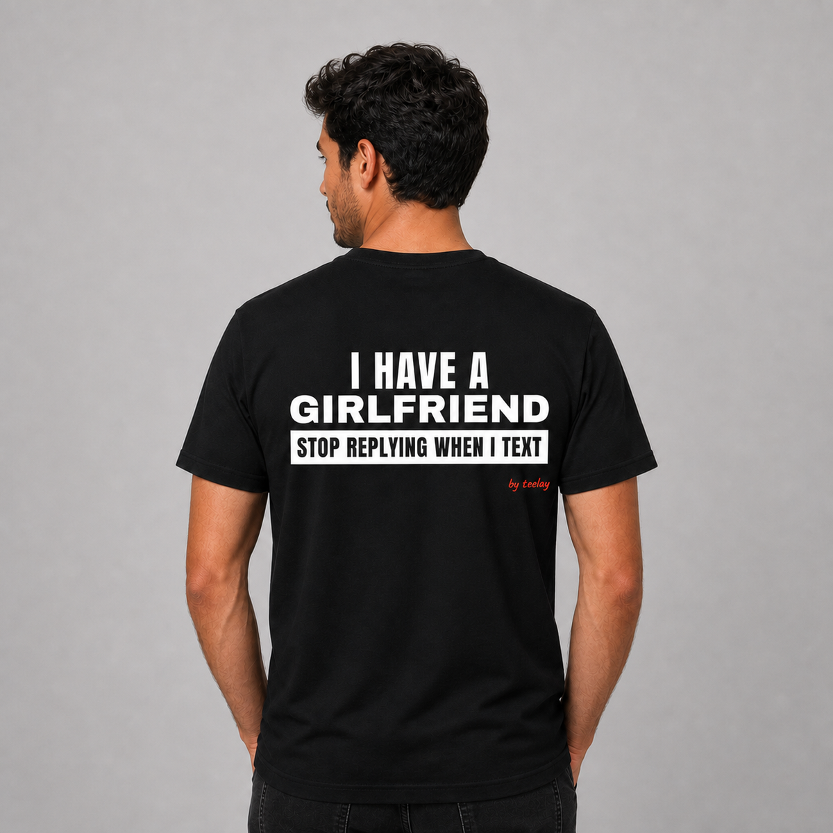 Man from behind wearing a black t shirt with I Have A Girlfriend Stop Replying When I Text printed on the back