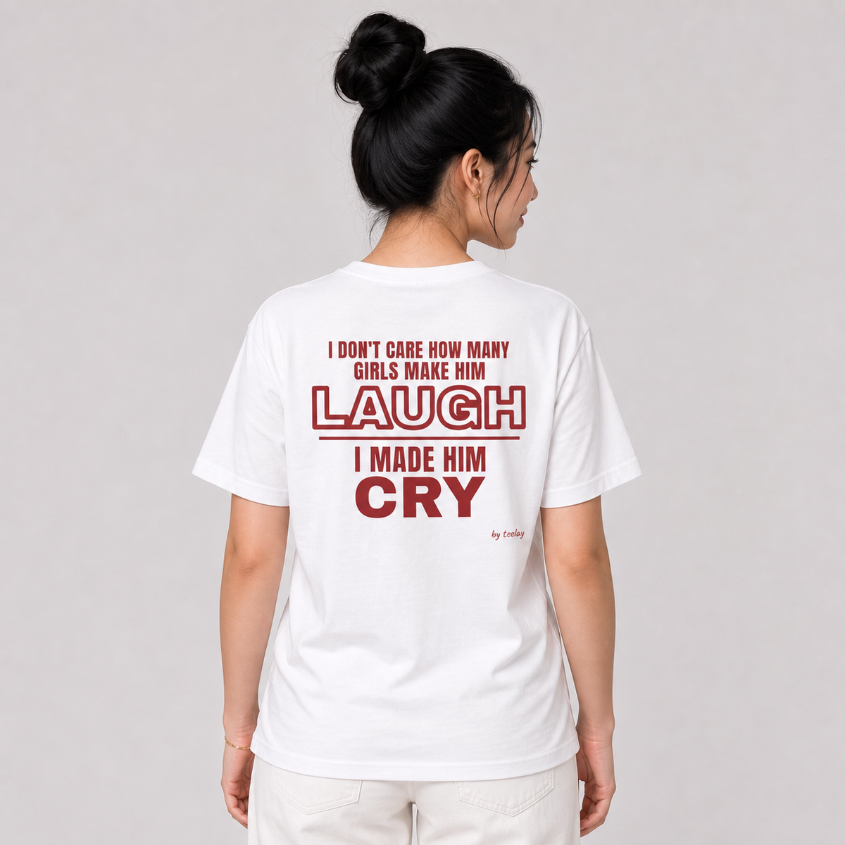 Woman from behind wearing a white t shirt with I Don't Care How Many Girls Make Him Laugh I Made Him Cry printed on the back