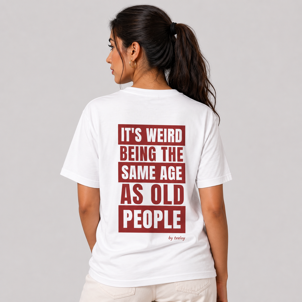 Woman from behind wearing a white t shirt with It's Weird Being The Same Age As Old People printed on the back