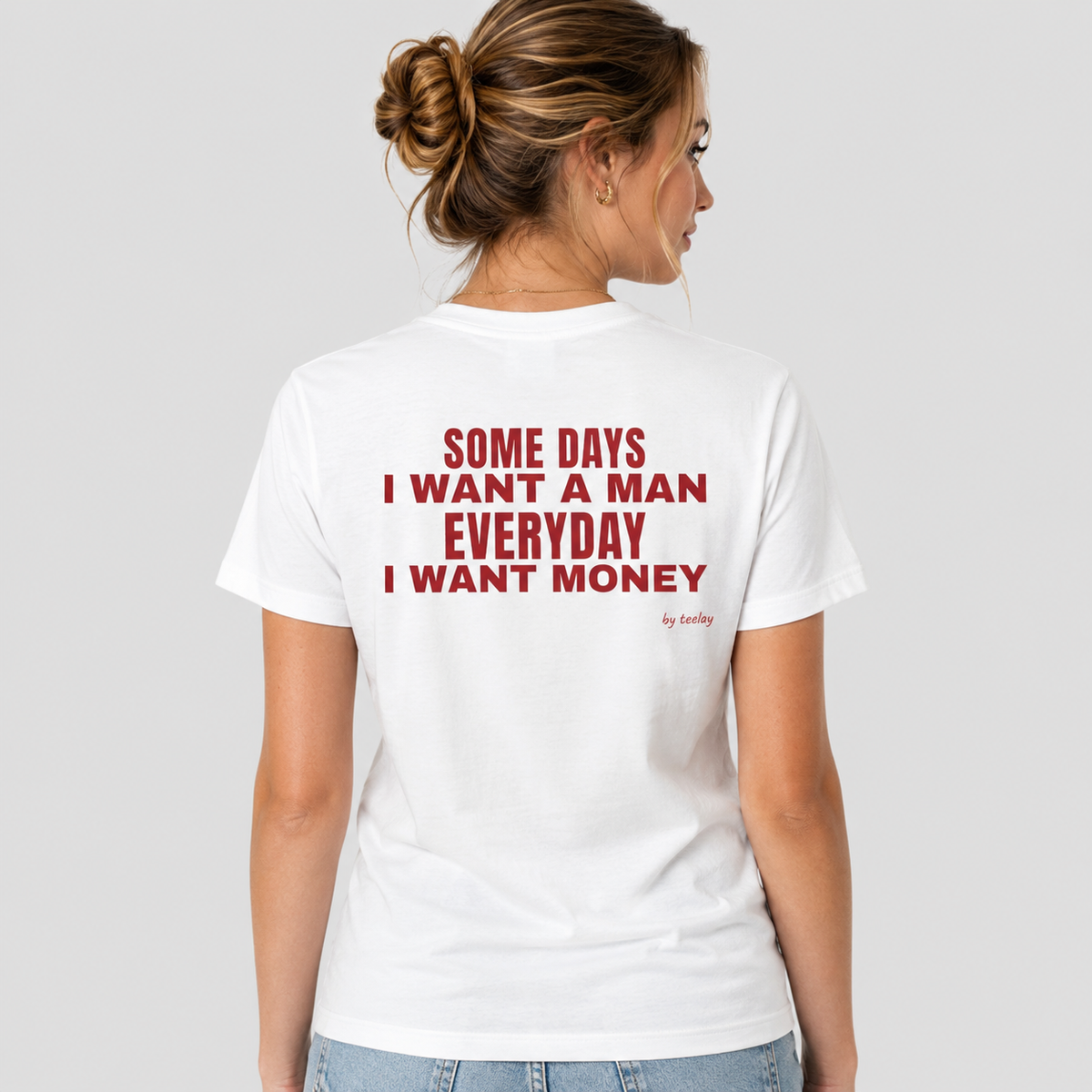 Woman from behind wearing a white t shirt with Some Days I Want A Man Everyday I Want Money printed on the back